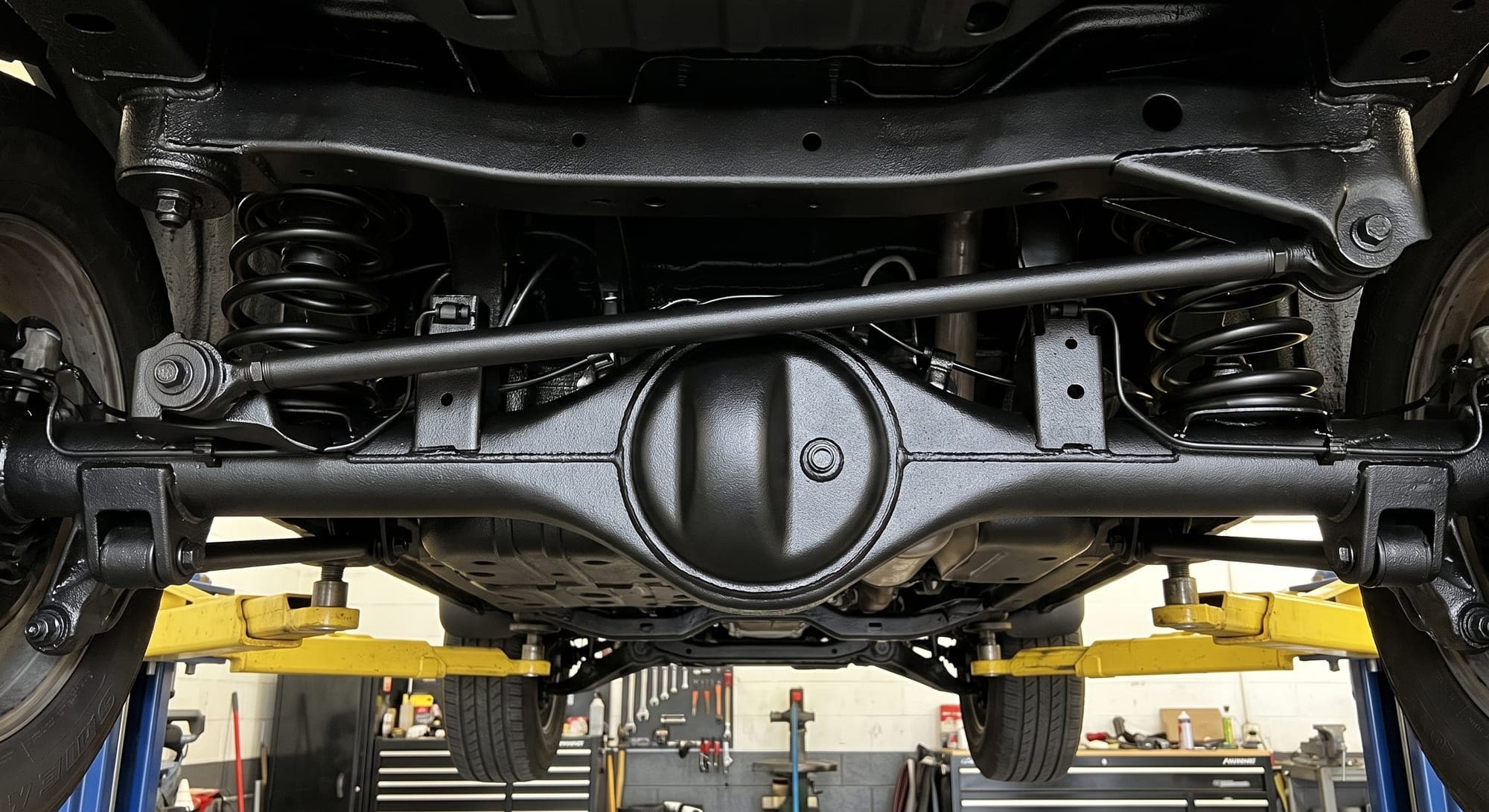 Rear axle, differential housing and coil springs freshly coated, seen from below on a two-post lift